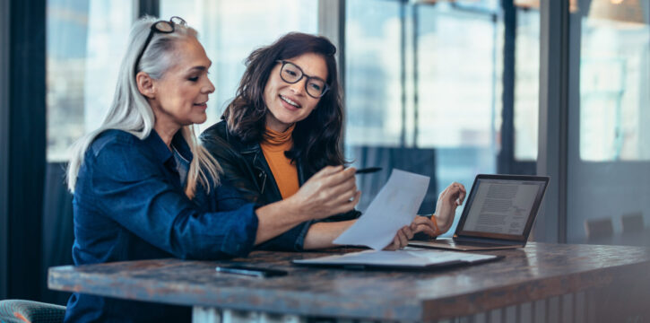 Two women analyzing documents while sitting on a table in office. Woman executives at work in office discussing some paperwork.